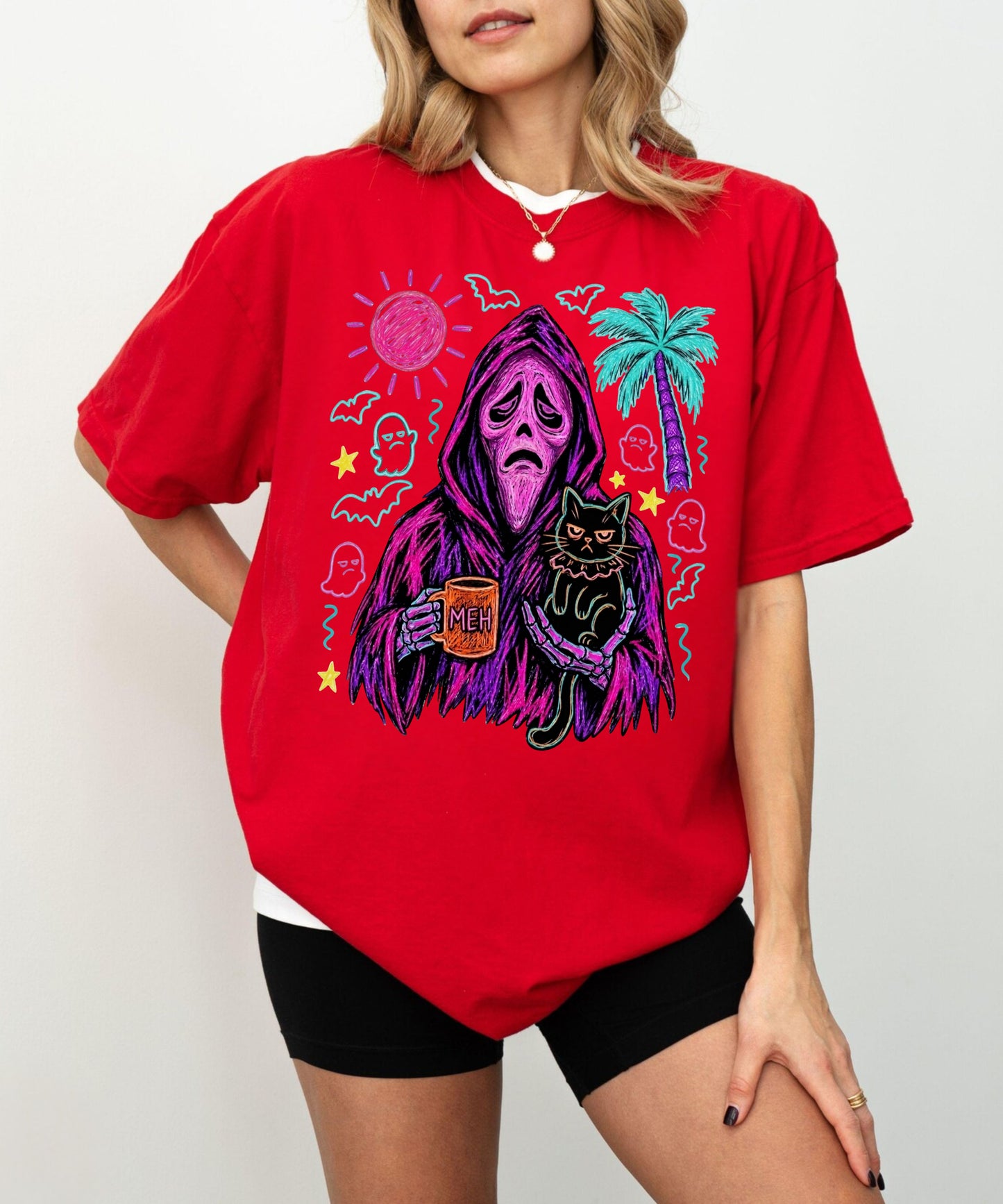 A woman wearing a bright red oversized graphic T-shirt with a horror-themed print featuring a hooded figure, a black cat, a palm tree, and spooky icons, paired with black shorts against a light gray background.