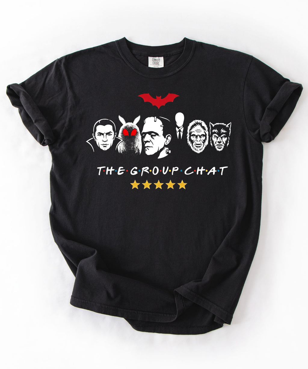 Black garment-dyed unisex t-shirt featuring The Group Chat horror monster squad graphic — Dracula, Mothman with red eyes, Frankenstein, Slender Man, Bigfoot, and Werewolf faces with red bat above and five gold stars below