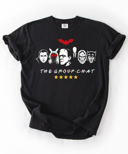 Black garment-dyed unisex t-shirt featuring The Group Chat horror monster squad graphic — Dracula, Mothman with red eyes, Frankenstein, Slender Man, Bigfoot, and Werewolf faces with red bat above and five gold stars below
