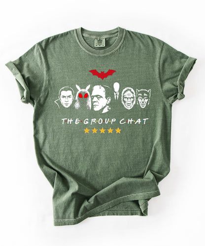 Moss garment-dyed unisex t-shirt featuring The Group Chat horror monster squad graphic — Dracula, Mothman with red eyes, Frankenstein, Slender Man, Bigfoot, and Werewolf faces with red bat above and five gold stars below