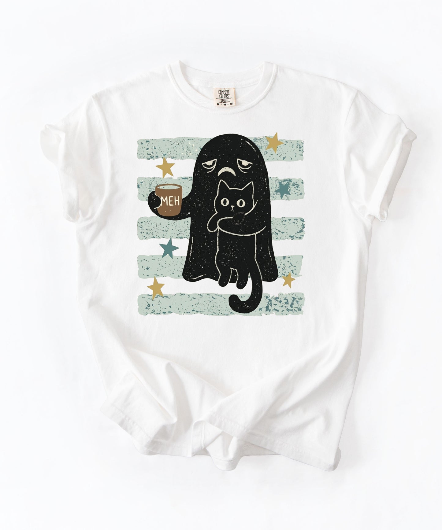 A white short-sleeve crewneck t-shirt with a graphic print of a black cat in a ghost costume holding a mug that says 'MEH', set against a background of distressed light green and white horizontal stripes with gold stars.