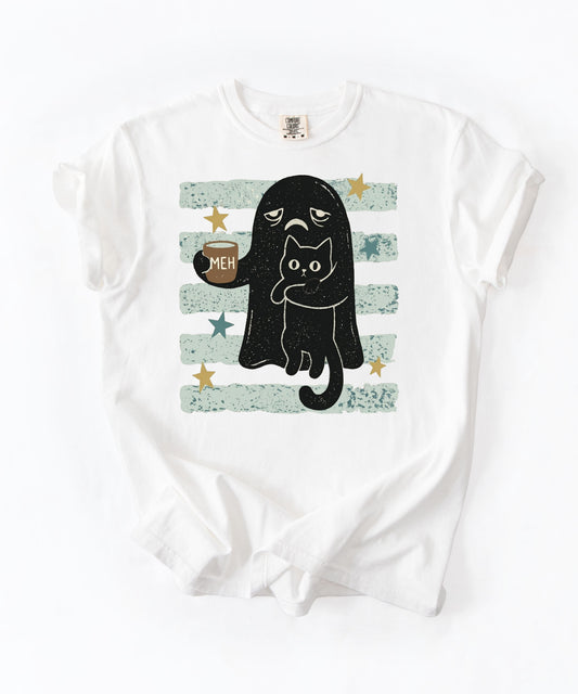 A white short-sleeve crewneck t-shirt with a graphic print of a black cat in a ghost costume holding a mug that says 'MEH', set against a background of distressed light green and white horizontal stripes with gold stars.