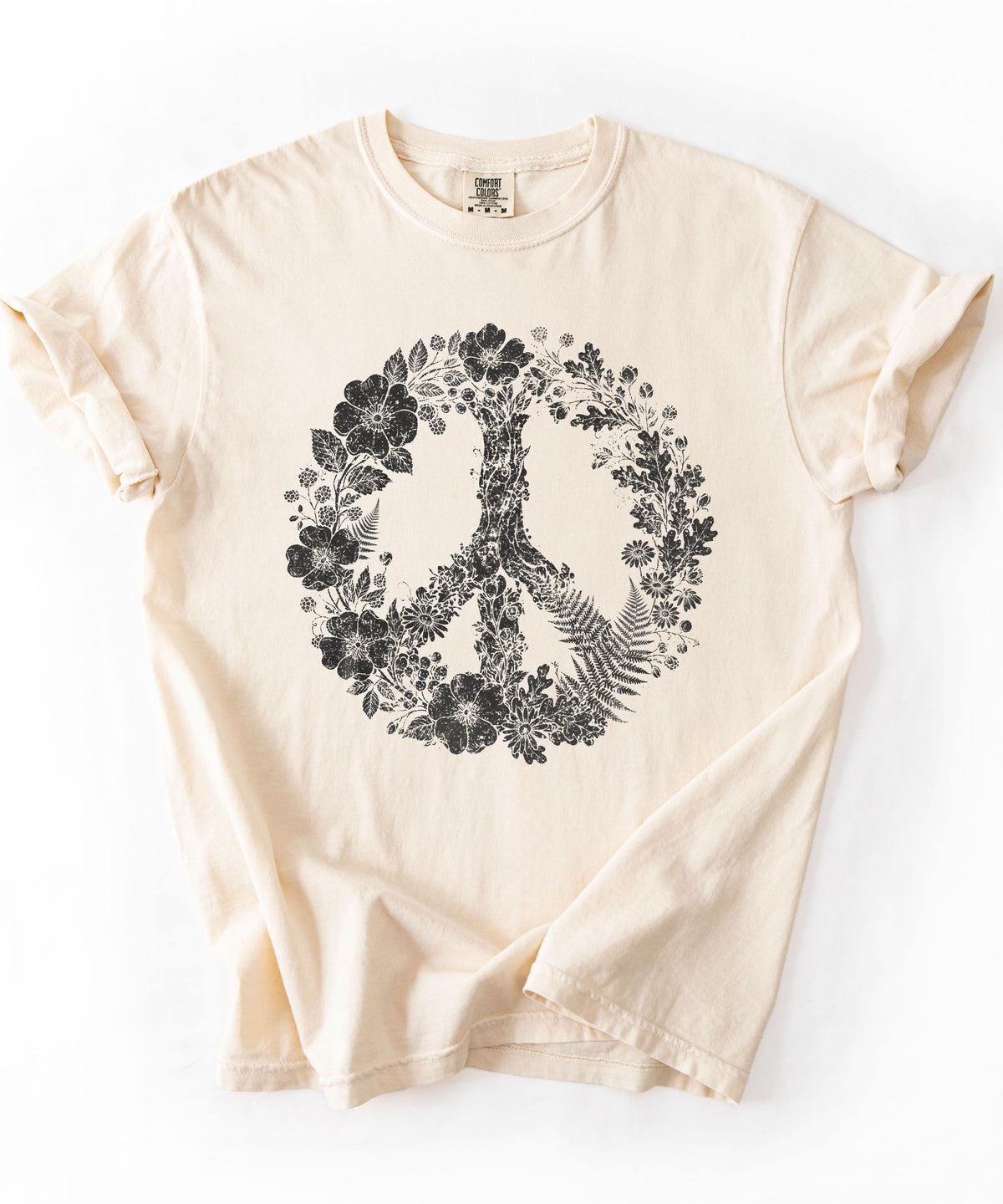 an Ivory colored short-sleeve t-shirt with a black peace sign graphic filled with floral and leafy patterns, laid flat against a white background.