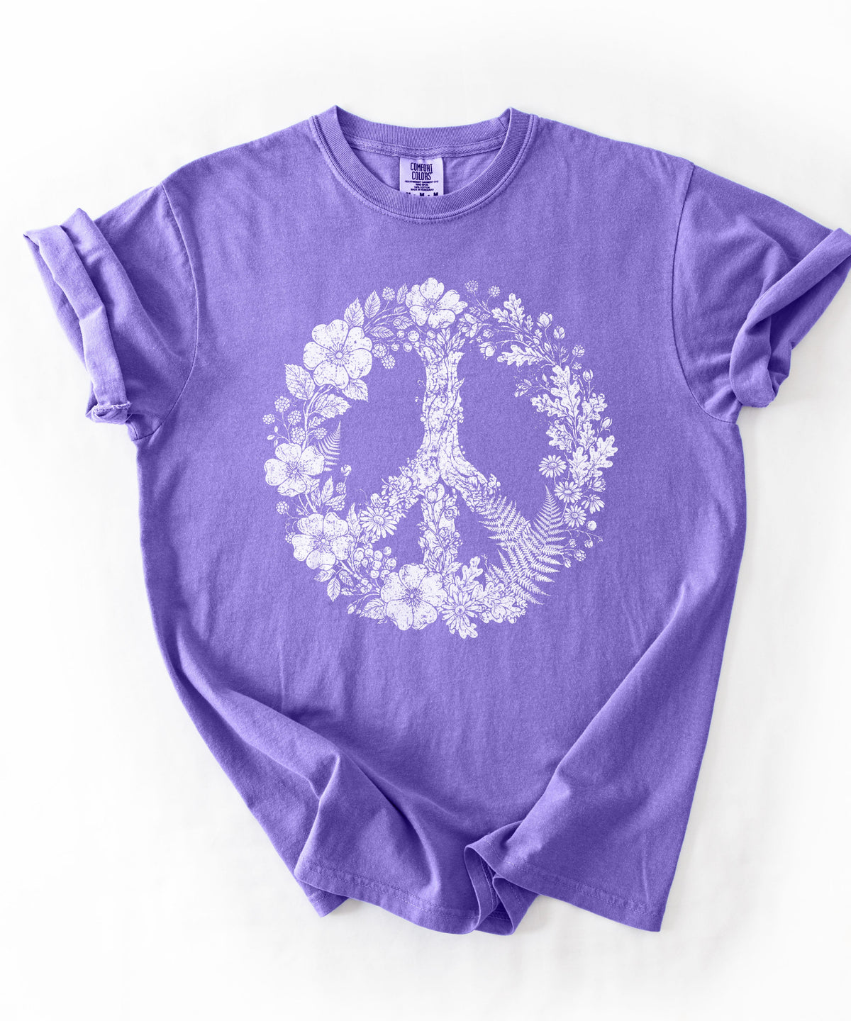 A Violet short-sleeve t-shirt with a white graphic of a peace sign formed by a tree and surrounded by flowers, laid flat on a white background.