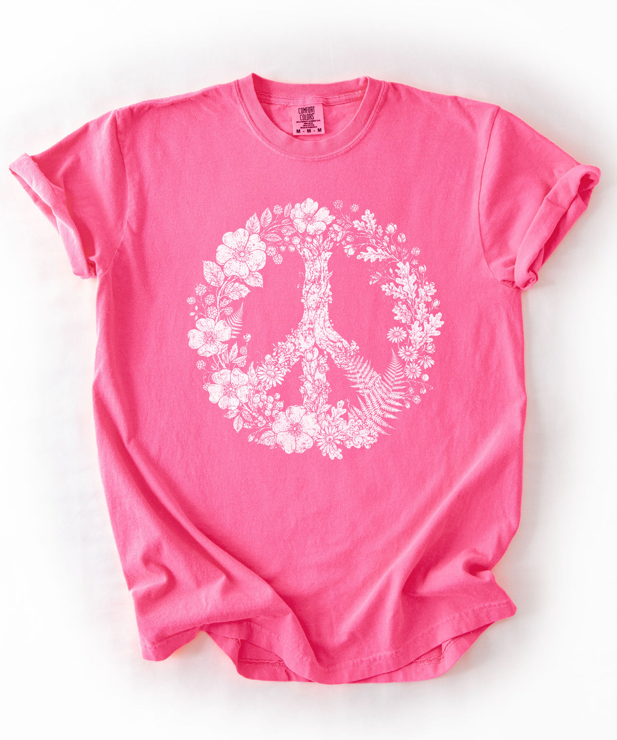 A Neon pink short-sleeve t-shirt with a white graphic of a peace sign made of flowers and leaves, laid flat on a white background.
