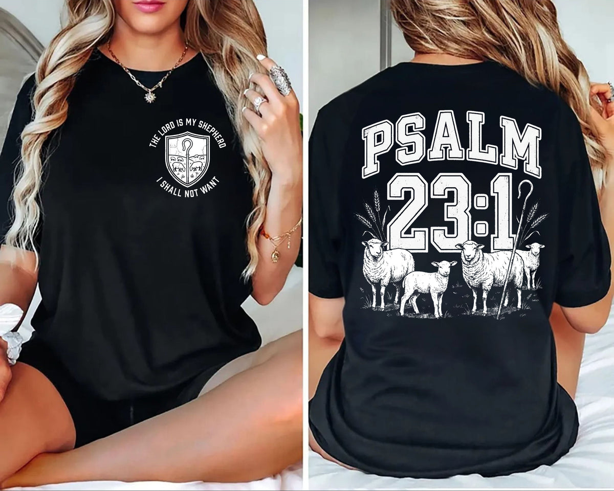 A black short-sleeve graphic T-shirt shown on a model from both the front and back. The front has a small white circular emblem with text, and the back features large white 'PSALM 23:1' lettering above an illustration of sheep.