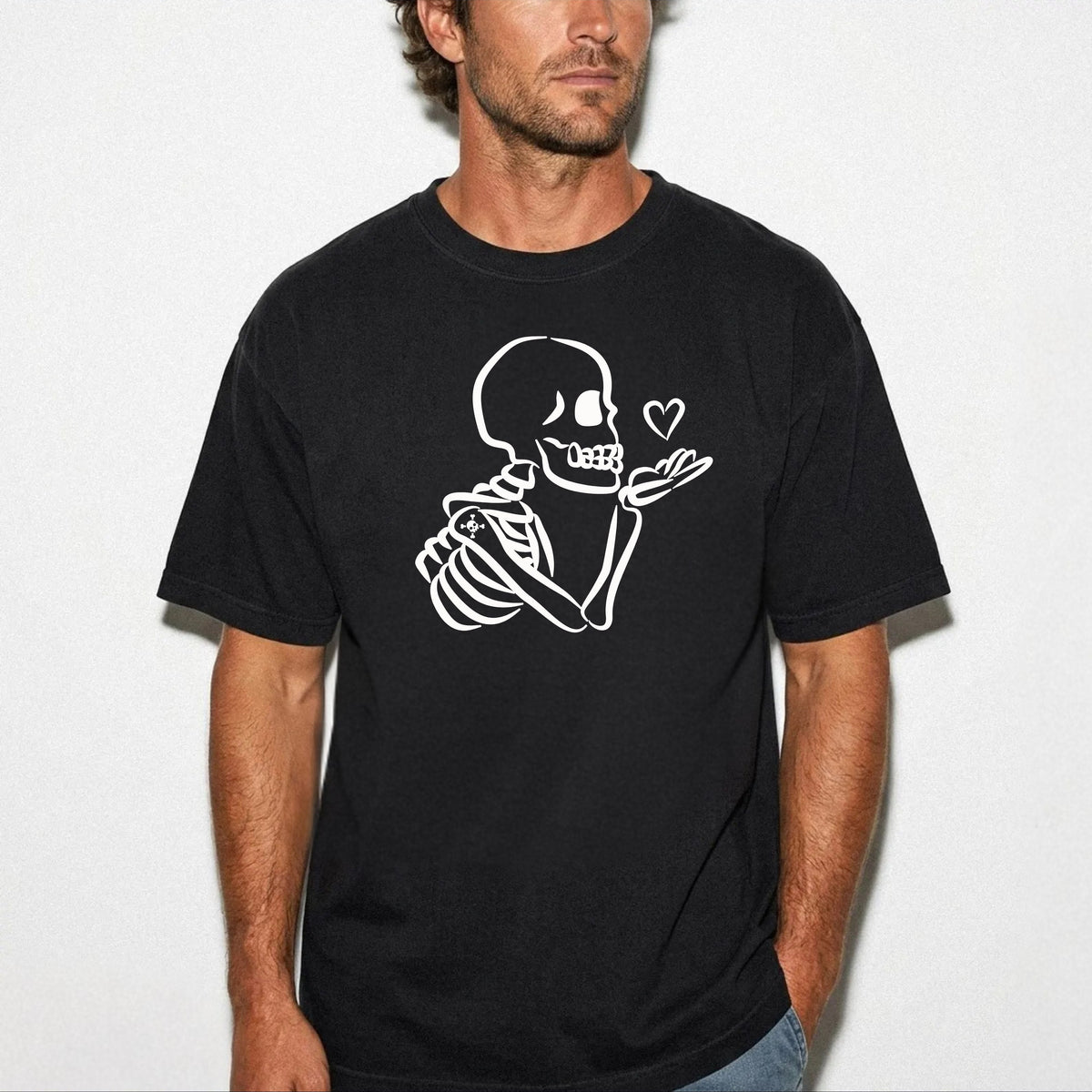 A man wearing a black crewneck t-shirt with a white line art graphic of a skeleton blowing a heart-shaped bubble, set against a plain light gray background.