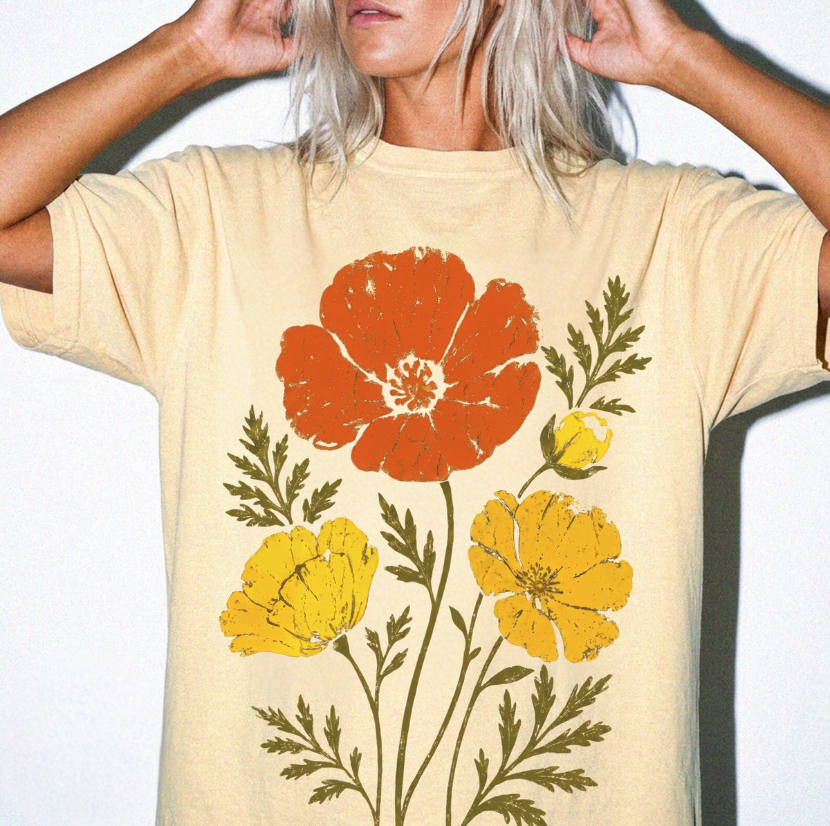 A person wearing a Butter-colored oversized T-shirt with a distressed graphic print of orange and yellow flowers with green leaves
