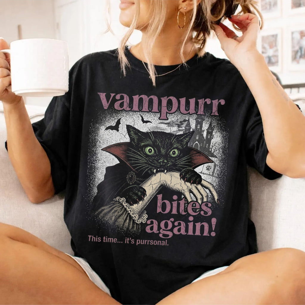 Funny Halloween cat shirt featuring a black cat in a vampire cape, bats, and the text “Vampurr Bites Again!