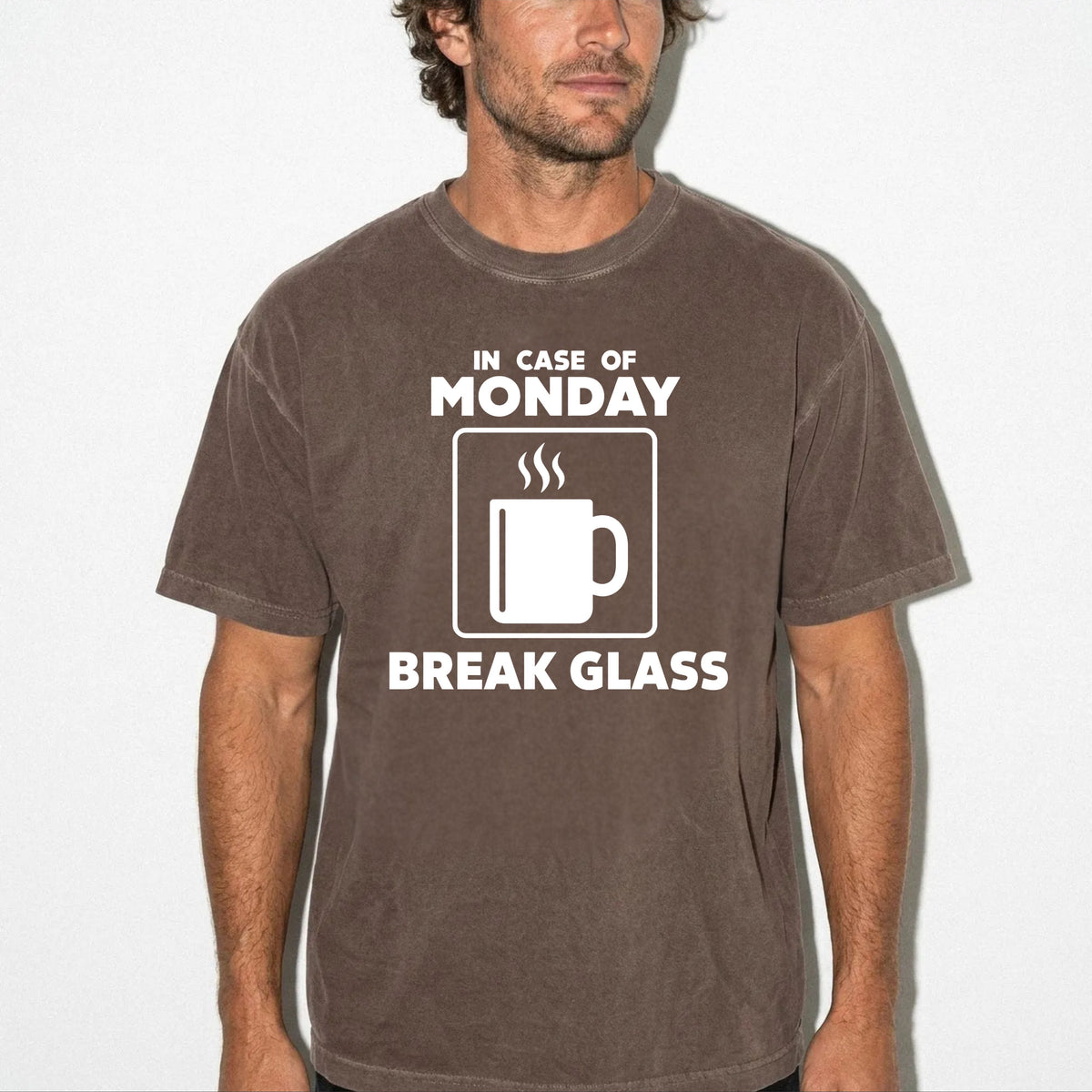 A man wearing an espresso colored-shirt with a white graphic that reads 'IN CASE OF MONDAY BREAK GLASS' with a coffee mug icon, shown against a plain white background.