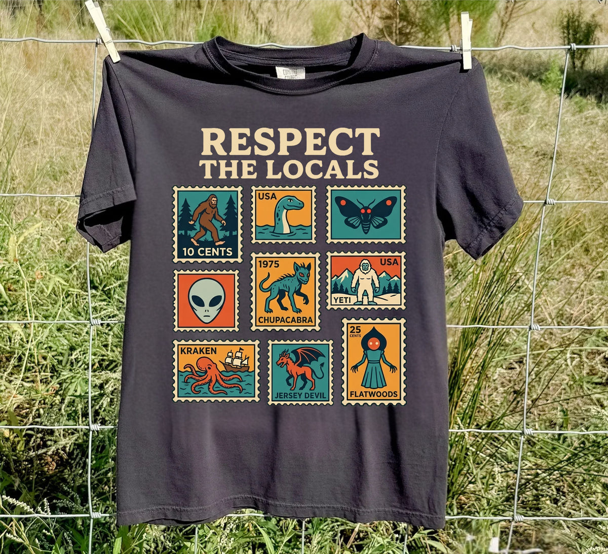 Black Respect the Locals cryptid T-shirt with colorful vintage monster stamps outdoors