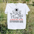 A white short-sleeve graphic T-shirt hanging on a wire fence outdoors. The shirt features a black line-art illustration of animals and a sun with the phrase 'protect the locals' in red script and black wavy lines below.