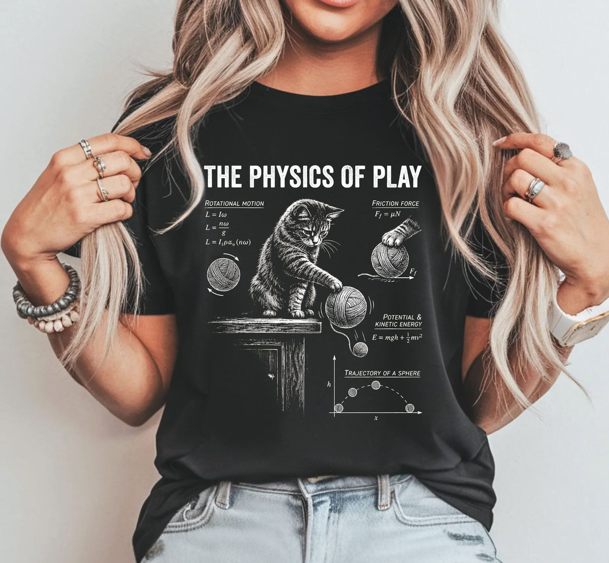 A woman wearing a black graphic t-shirt with a white print of a cat and physics equations, paired with light wash jeans, set against a plain light gray background.