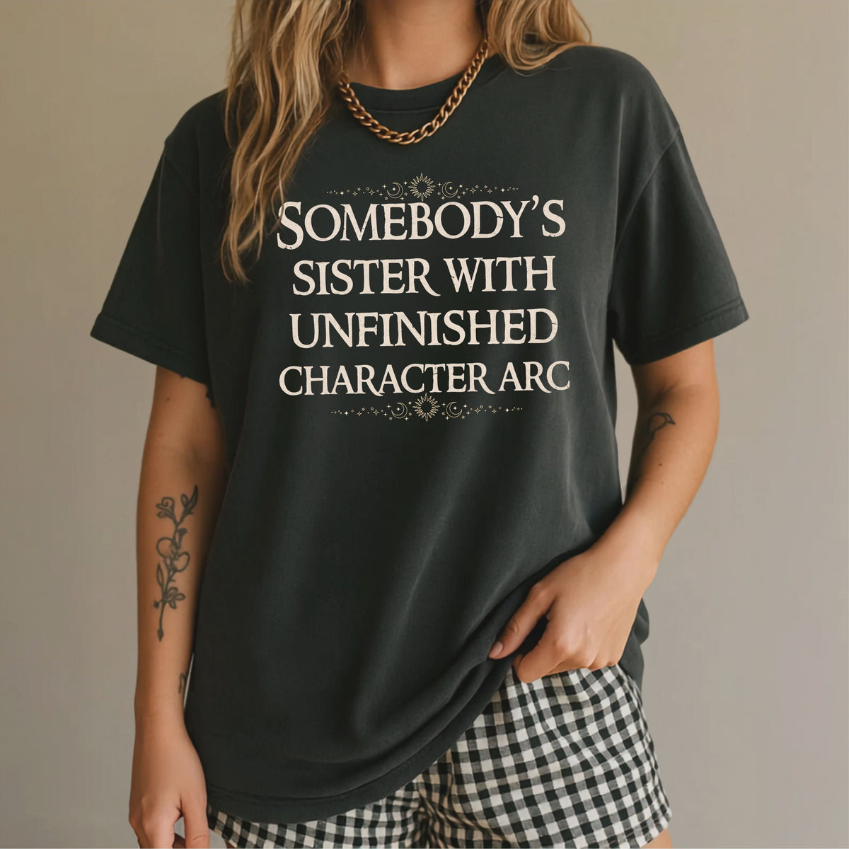 Black T-shirt with “Somebody’s Sister with Unfinished Character Arc” lettering and celestial accents.