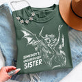 Moss Comfort Colors shirt featuring a female knight riding a dragon with her sword raised and the phrase ‘Somebody’s Unsupervised Sister.