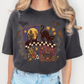 A Pepper colored short-sleeve t-shirt with a detailed Halloween graphic print on the front, featuring a black cat, bats, a cauldron, and the word 'BOO' on a white background.