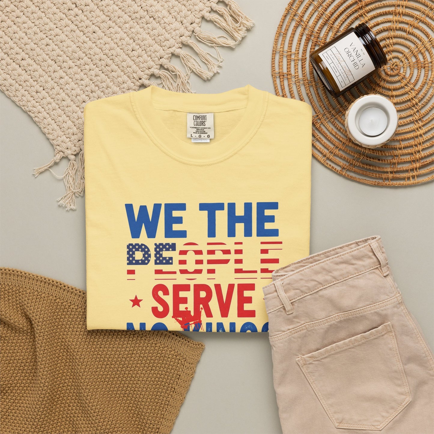 Yellow t-shirt with 'We the People Serve Nothing' text on a neutral surface with accessories.