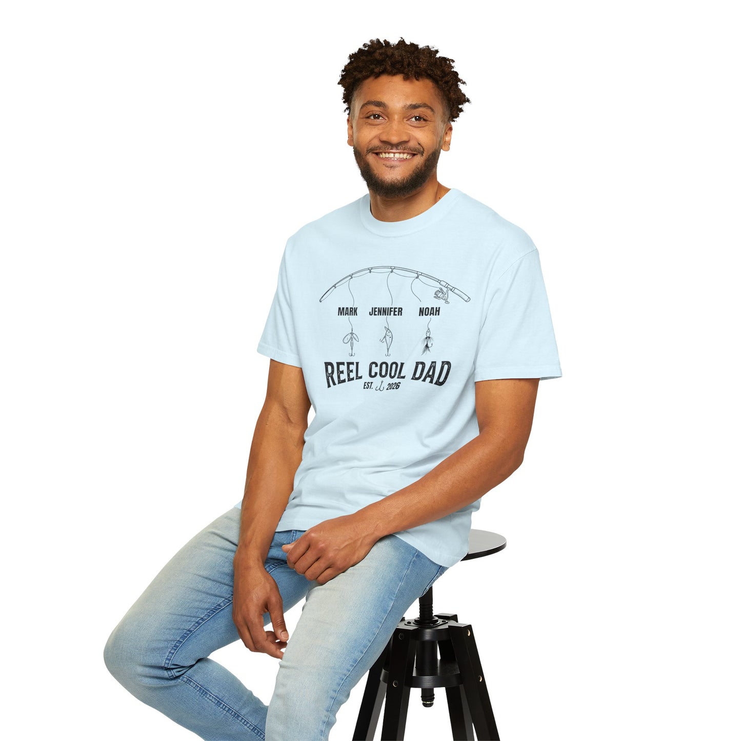 Man sitting on a stool wearing a Chambray blue t-shirt with text and light blue jeans on a white background