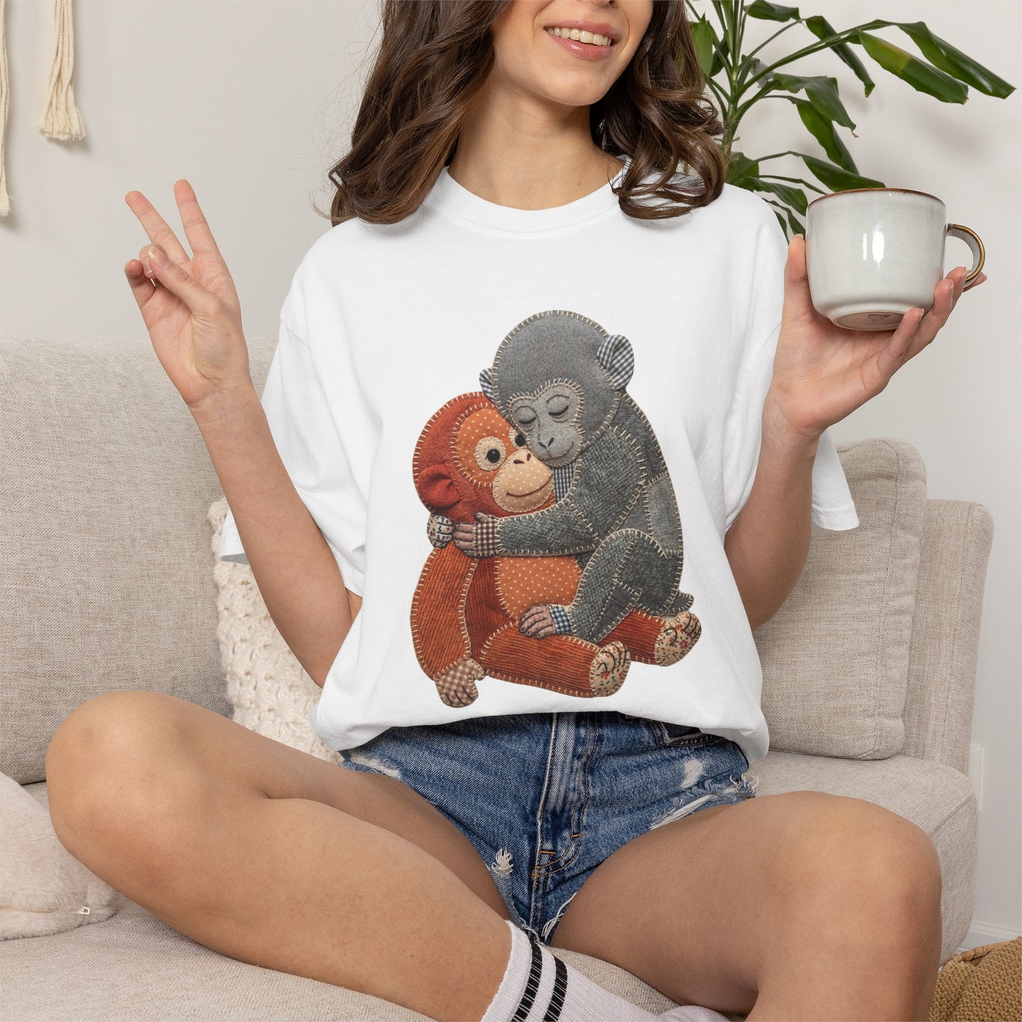 Person wearing a white t-shirt with monkey design, sitting on a couch holding a mug.