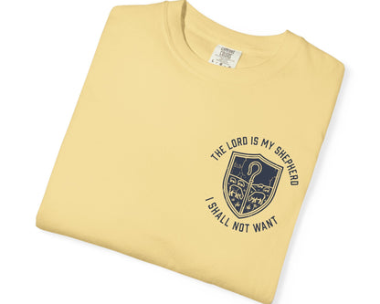 A folded butter yellow t-shirt with a navy blue graphic on the chest. The graphic features a shield with a shepherd and the text 'THE LORD IS MY SHEPHERD I SHALL NOT WANT'.