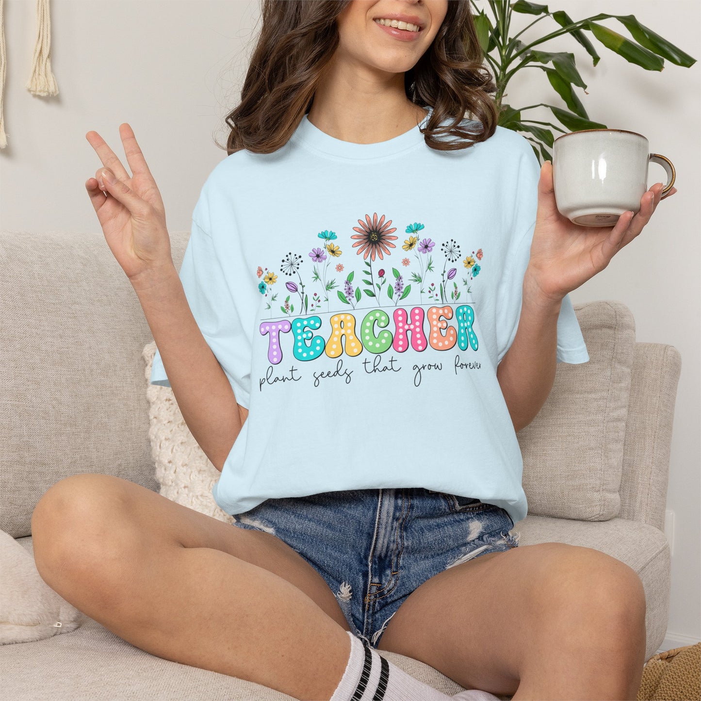 Person wearing a chambray blue t-shirt with a graphic and text, sitting on a couch holding a mug.