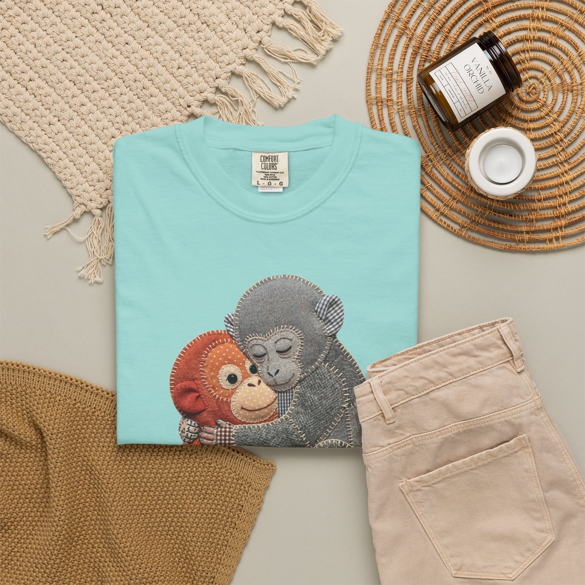 Folded chalky mint t-shirt with monkey design on a neutral surface with accessories.