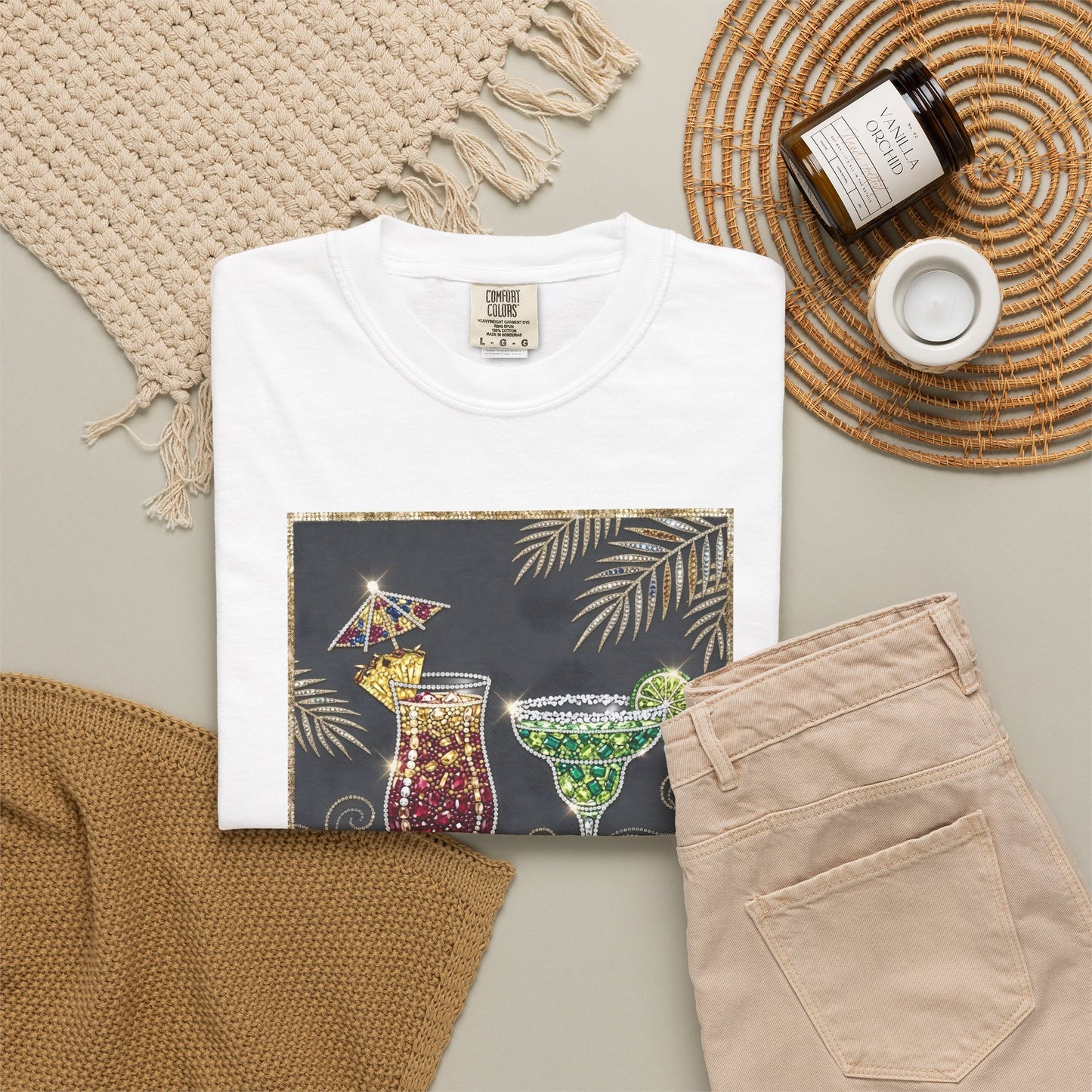 White t-shirt with cocktail graphic, beige pants, and decorative items on a neutral background