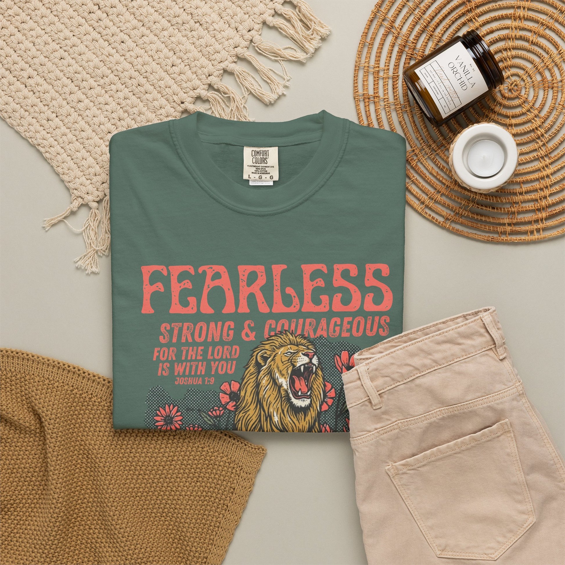 blue spruce t-shirt with 'Fearless Strong & Courageous' text and lion graphic on a neutral surface with accessories.