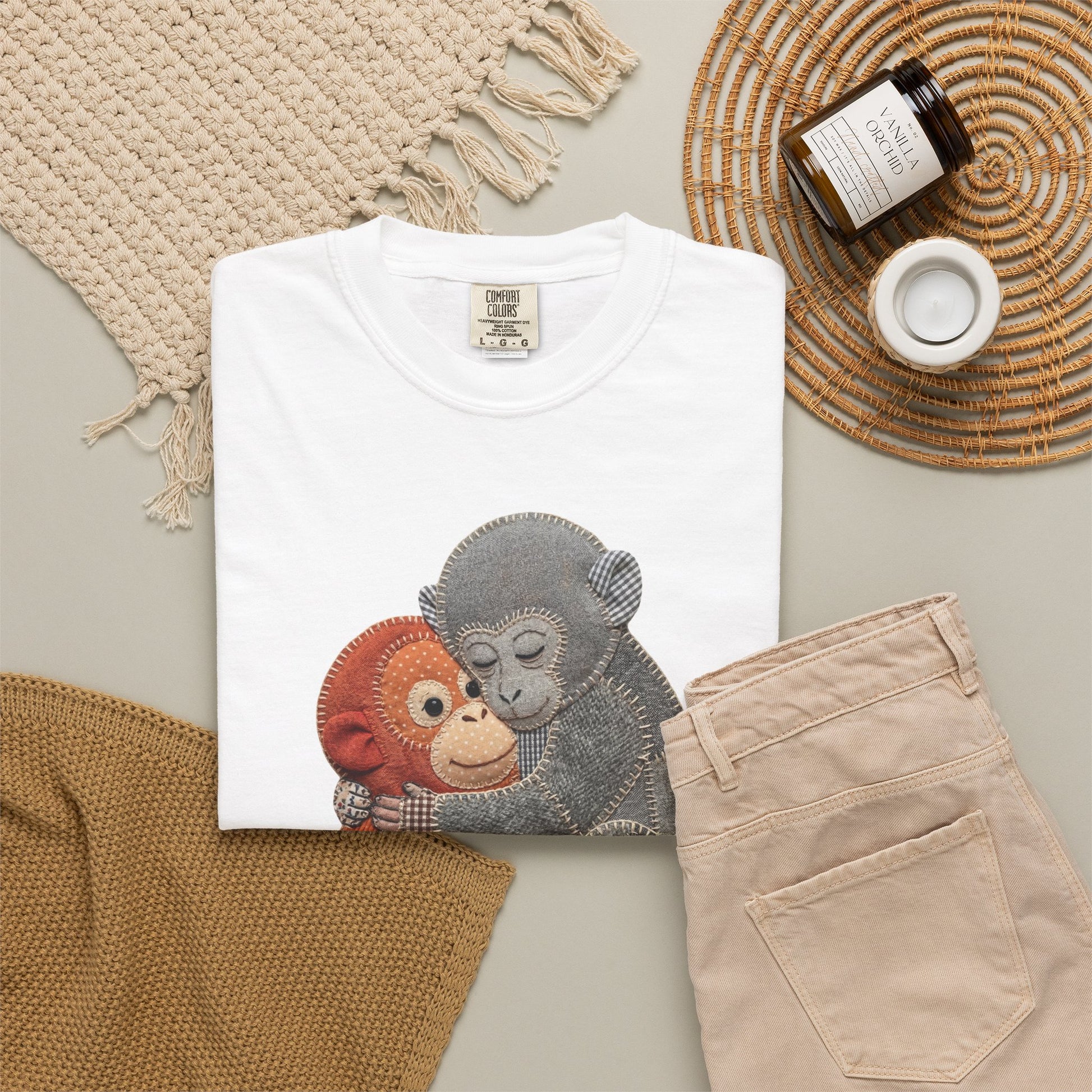 White t-shirt with monkey design on a neutral surface with beige pants and decorative items.
