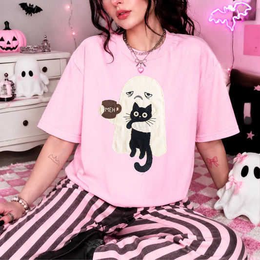 A person wearing a Blossom pink oversized T-shirt with a black cat and white ghost graphic, paired with pink-and-black striped pants, posed in a Halloween-themed room with ghost decorations and pink lighting.